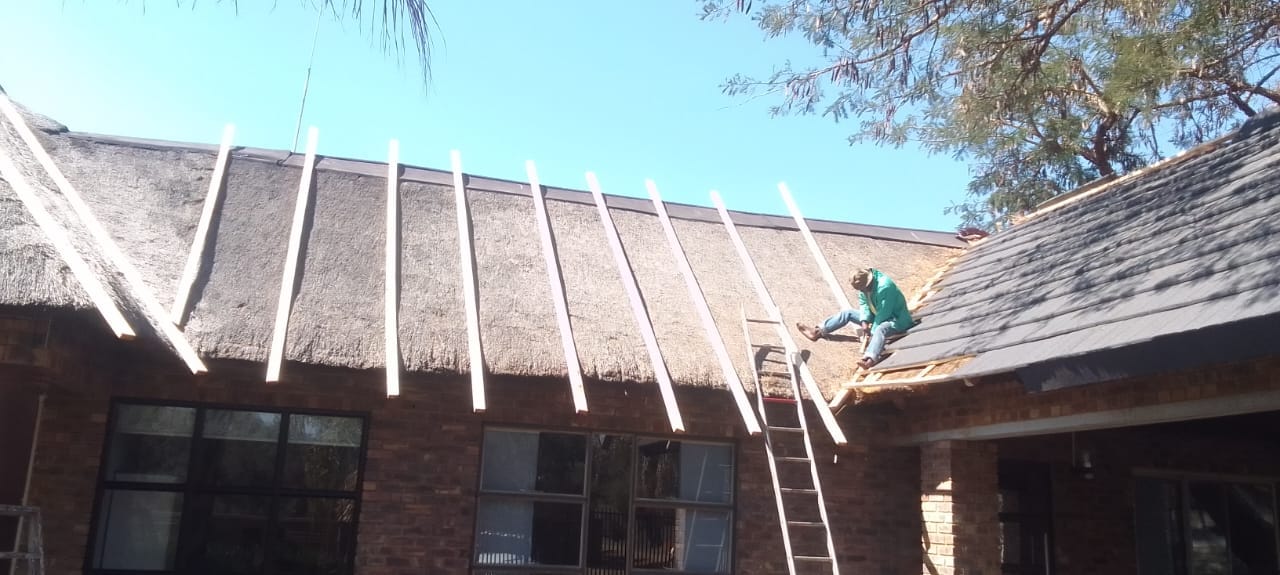 Roofing team working on an existing thatched roof during repair work